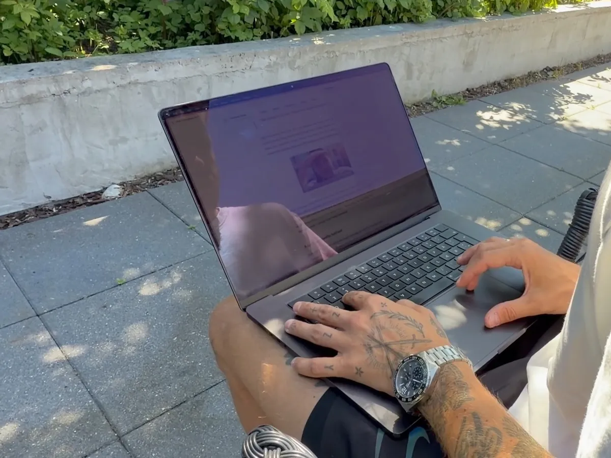 A MacBook Pro screen in the sun on a terrace with Outshine off: the page is dim and the screen mostly reflects